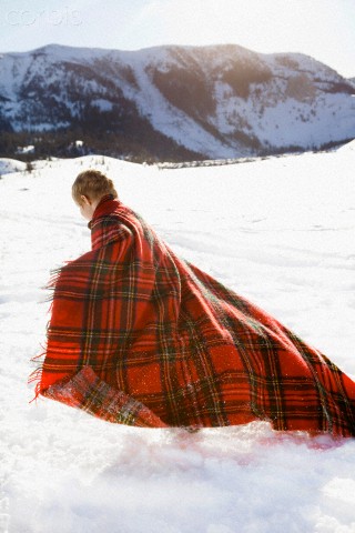 Young boy wrapped in red plaid blanket playing in snow